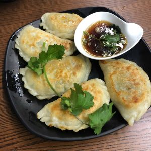 Five half-circle shaped chive pan-fried dumplings arranged on a black plate with a white bowl of dipping sauce